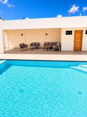 Una piscina con acqua cristallina e di colore blu, circondata da un edificio bianco con una porta in legno e due finestre.