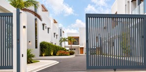 Una zona residencial moderna con entrada vigilada, edificios blancos y abundante vegetación bien cuidada.