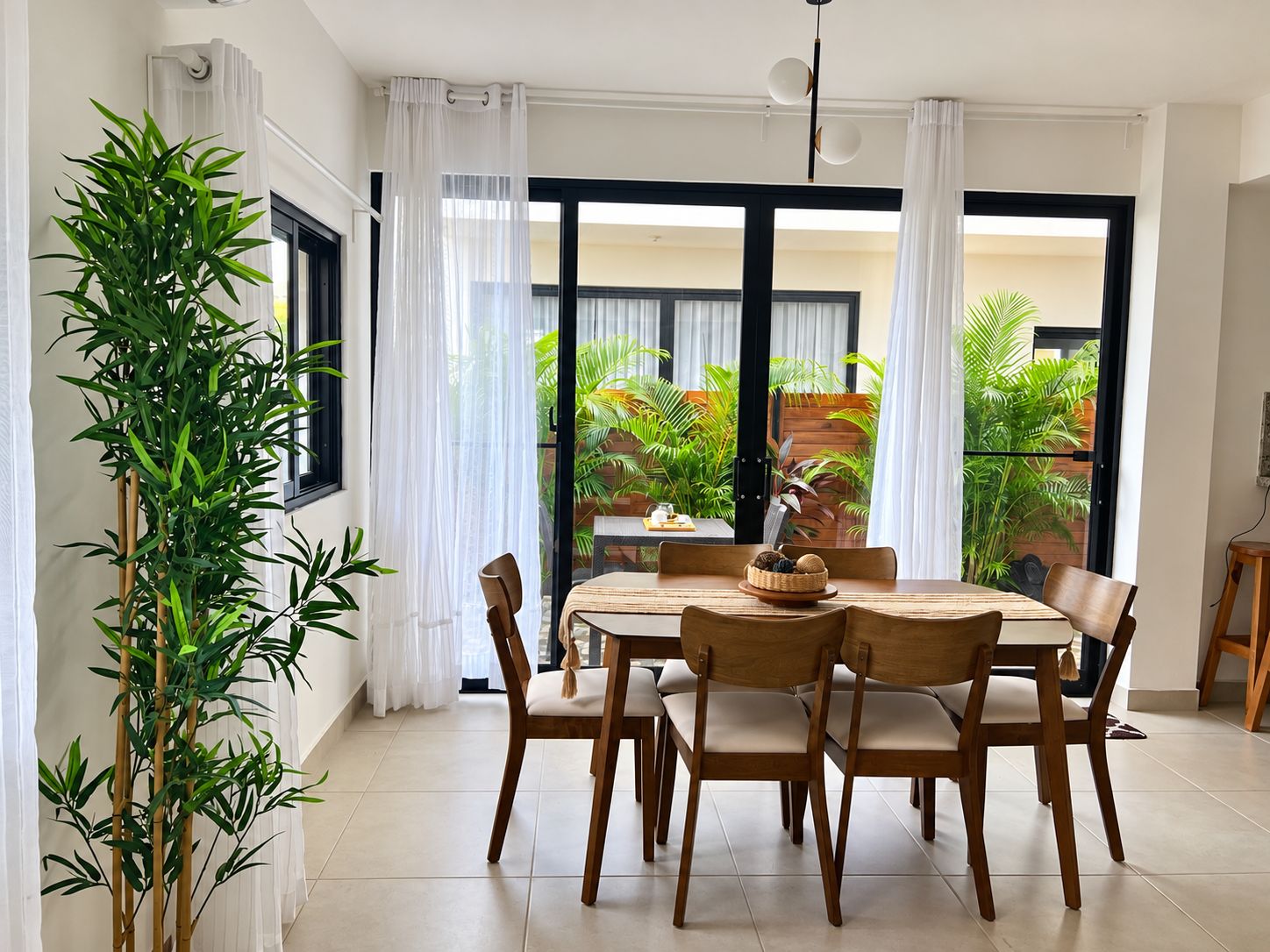 A dining area with a table and chairs, a large potted plant, and a view of a garden through a glass door.