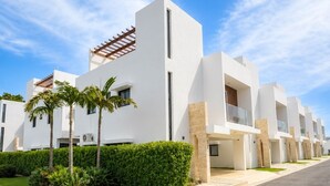 A modern residential building with a white facade, multiple balconies, and a well-maintained garden with palm trees. - Caribbean getaway,  minutes away from the airport,  Downtown Punta Cana, beaches and attractions. Whether you're here for adventure, romance, great family time or pure relaxation, this is the place where memories are made. (Punta Cana)
