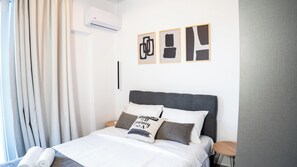 Ein modernes Hotelzimmer mit Bett, Nachttisch, Wandklimaanlage und abstrakter Kunst an der Wand.