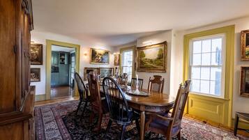 Une salle à manger avec une table en bois, des chaises et un tapis. Les murs sont ornés de tableaux et il y a une fenêtre avec un cadre jaune.