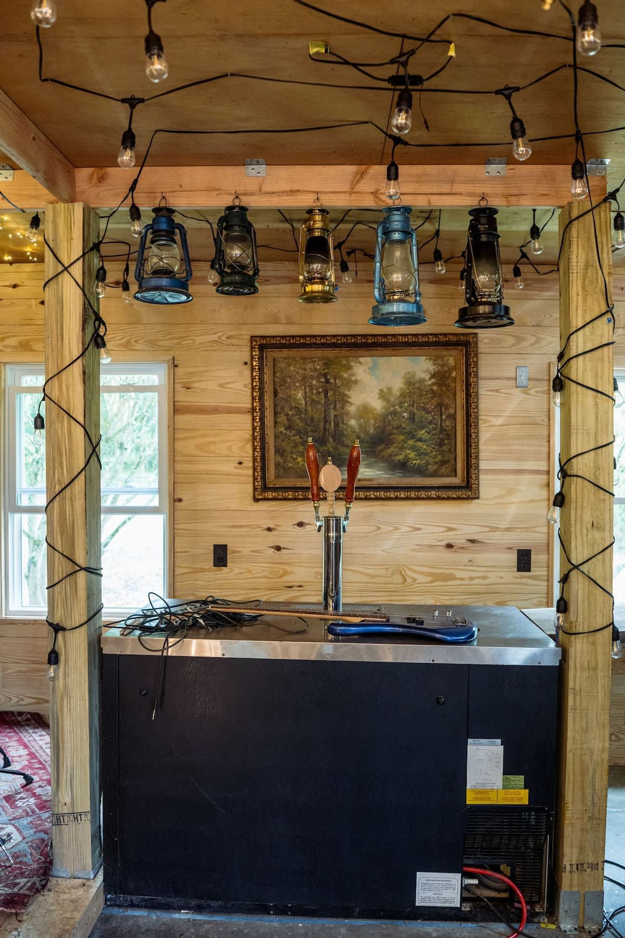 Un rústico espacio de bar con paredes de madera, un cuadro y una mezcla de luces colgantes y faroles.