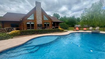 A log cabin with a stone chimney, a swimming pool, and outdoor seating.