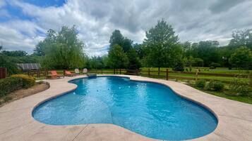 A swimming pool with a curved edge, surrounded by a wooden fence, and a grassy area with trees in the background.