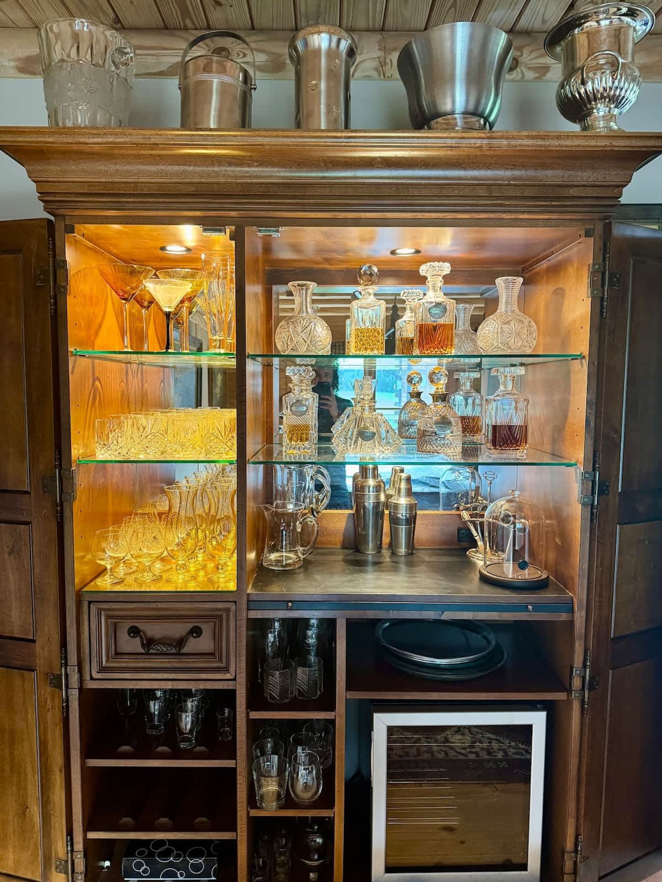 A wooden cabinet with glass shelves displaying various glassware and bottles.