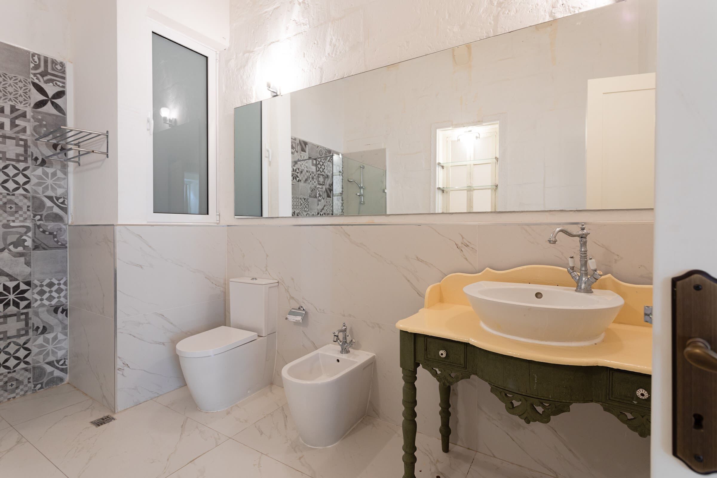 Un baño con bidé, inodoro y lavamanos con espejo superior.