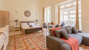 Een slaapkamer met een bed, nachtkastjes, een bank, een eettafel met stoelen en een vloer met een patroon.
