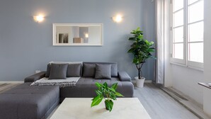A modern living room with a grey sofa, a white coffee table, and a large potted plant. - Valletta Exclusive 3BR House with Rooftop Terrace (Valletta)