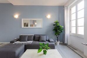 A modern living room with a grey sofa, a white coffee table, and a large potted plant. - Valletta Exclusive 3BR House with Rooftop Terrace (Valletta)