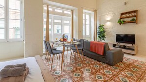 A compact living space with a bed, a dining area, a sofa, a TV, and a small plant. - Valletta Exclusive 3BR House with Rooftop Terrace (Valletta)