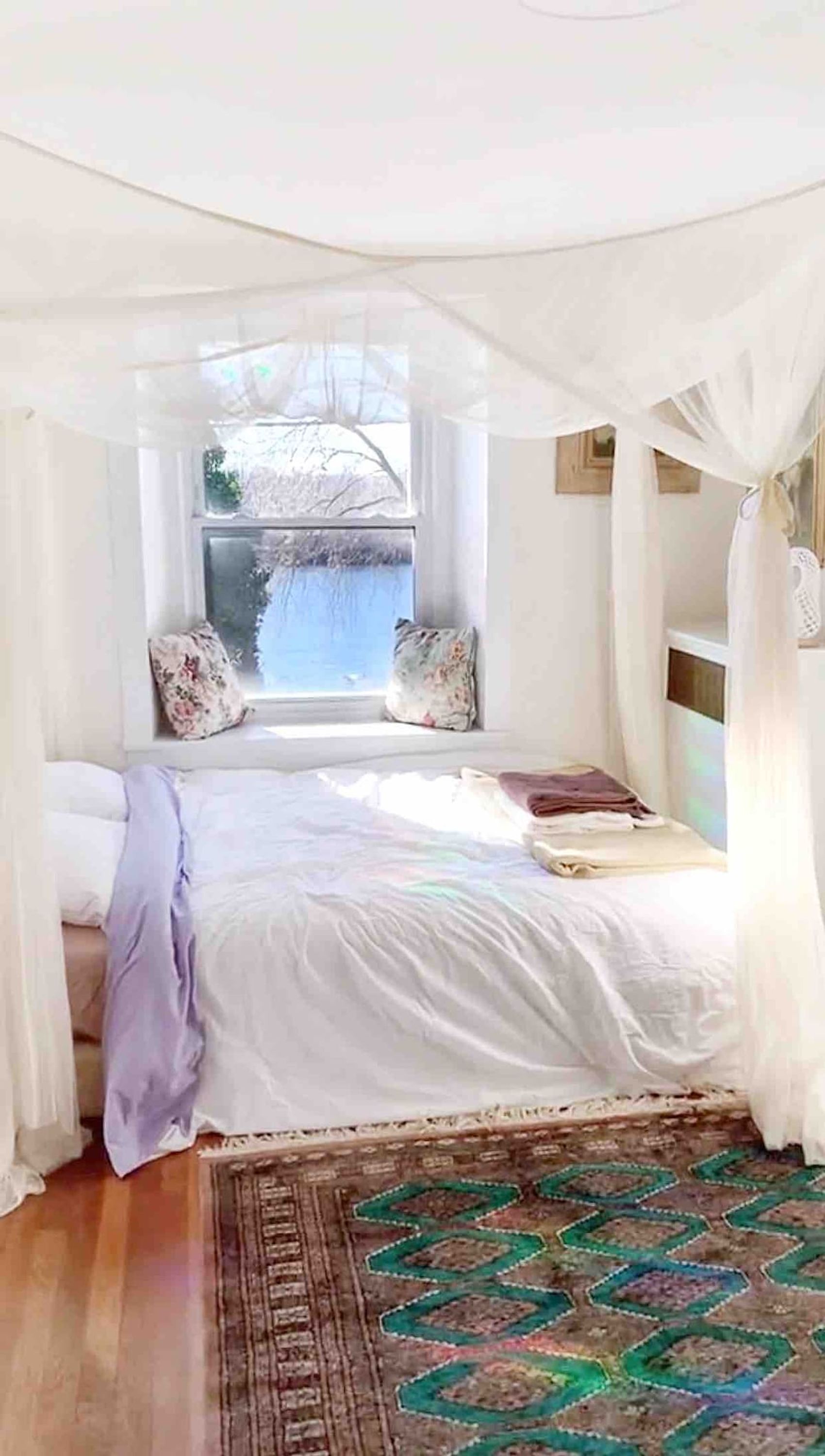 A bedroom with a canopy bed, a view of trees through the window, and a patterned rug. - Charming   Whimsical Historic River Home (Hopewell Township)
