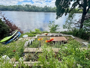 Un patio junto al lago con una mesa y sillas, rodeado de follaje y vistas al lago.