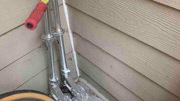 Un vélo avec un guidon rouge et un cadre en métal, appuyé contre un mur en bois.