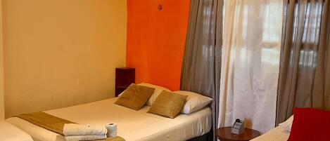 A hotel room with two beds, a small table, and a window with curtains.