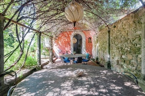 A covered outdoor area with a stone wall, a table with chairs, and a hanging light fixture. - Elegant room in 15th-century villa with private bathroom and pool (Grassina)