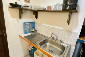 A compact kitchen with a stainless steel sink, a blue dish rack, and a shelf above holding dishes and cookware. - 05 Conchi abajo in Isla Mujeres (Isla Mujeres)