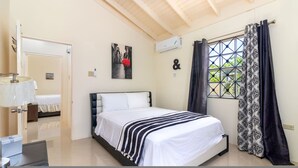 Un dormitorio con cama, una ventana con cortinas estampadas, aire acondicionado de pared y un cuadro.