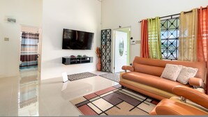 Una sala de estar moderna con un sofá de cuero, un televisor de pantalla plana y un amplio ventanal con cortinas.