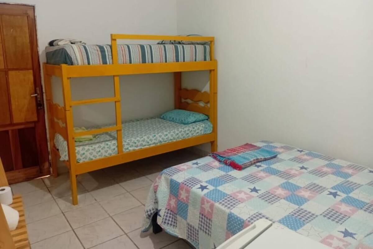 A bunk bed with a lower bunk and a single bed with a quilt. There is a wooden wardrobe and a toilet visible.