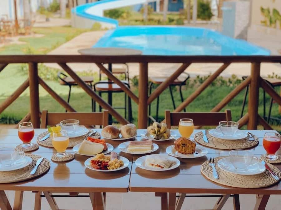 A dining table set with breakfast items, including plates, glasses, and a pool in the background.
