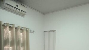 Ein kleines, sauberes Zimmer mit einem Bett, einem Vorhang und einer Klimaanlage.