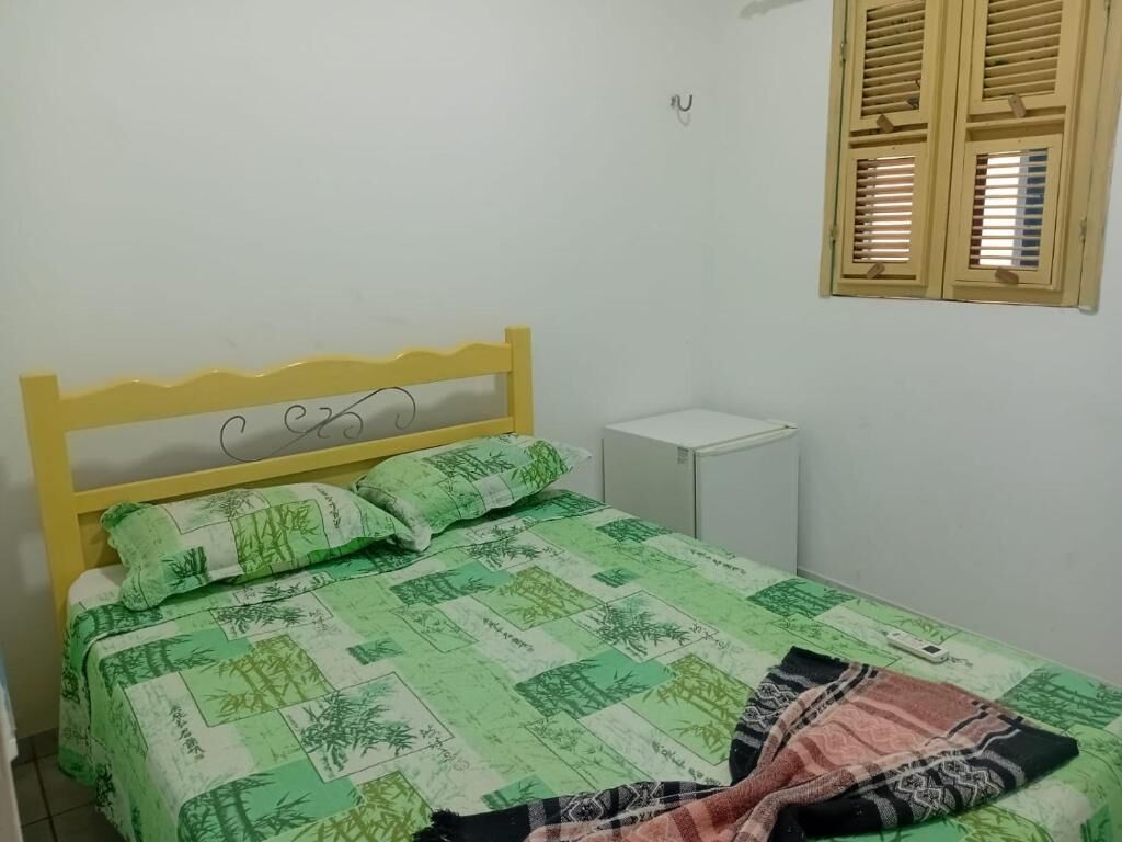 A single bed with a green and white patterned bedspread, a wooden headboard, and a bedside table.