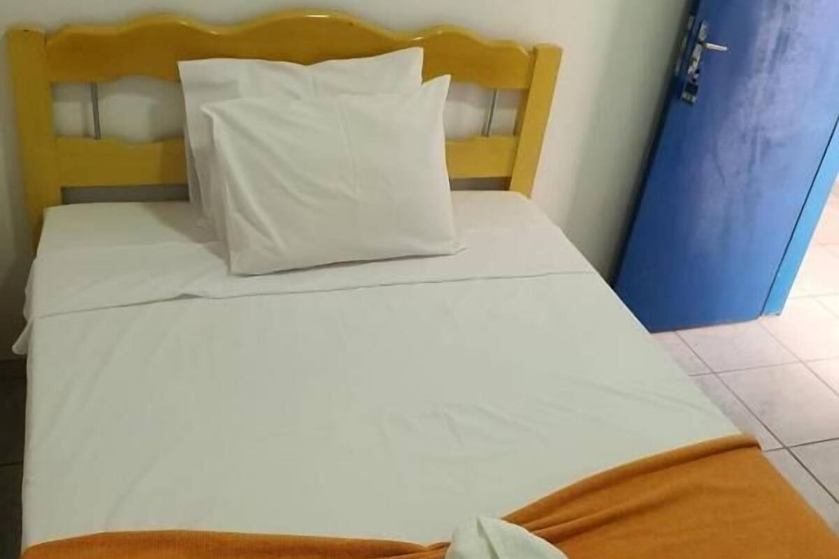 A bed with a yellow headboard, white bedding, and an orange blanket.