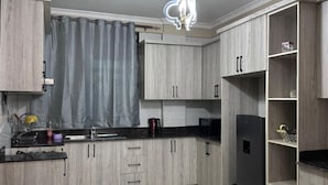 Een moderne keuken met lichte houten kastjes, een zwart aanrecht en een ingebouwde zwarte koelkast.
