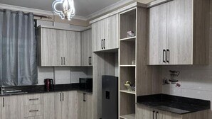 Een moderne keuken met lichte houtkleurige kastjes, een zwart aanrecht en een ingebouwde koelkast.