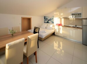 A modern, compact room with a bed, a dining table with chairs, a small kitchen area, and a painting on the wall. - Two-bedroom family rooms apartment Grey Goose 14 with balcony and sea view (Novalja)