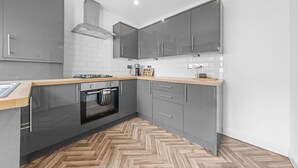 Une cuisine moderne avec des armoires grises, un plan de travail en bois, un four encastré et un sol à motifs en chevrons.
