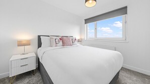 Une chambre moderne avec un grand lit, une table de chevet avec une lampe et une fenêtre donnant sur le ciel.