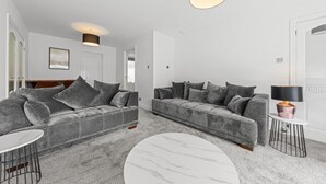 Un salon moderne avec deux canapés gris, une table basse en marbre et une petite table d’appoint avec une lampe.