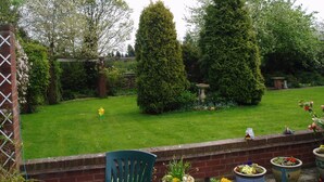 A garden with a lawn, a brick wall, and a blue chair. - Coppers End Guest House (Lichfield)