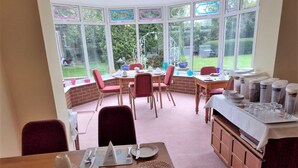 A dining area with a view of a garden through large windows. - Coppers End Guest House (Lichfield)