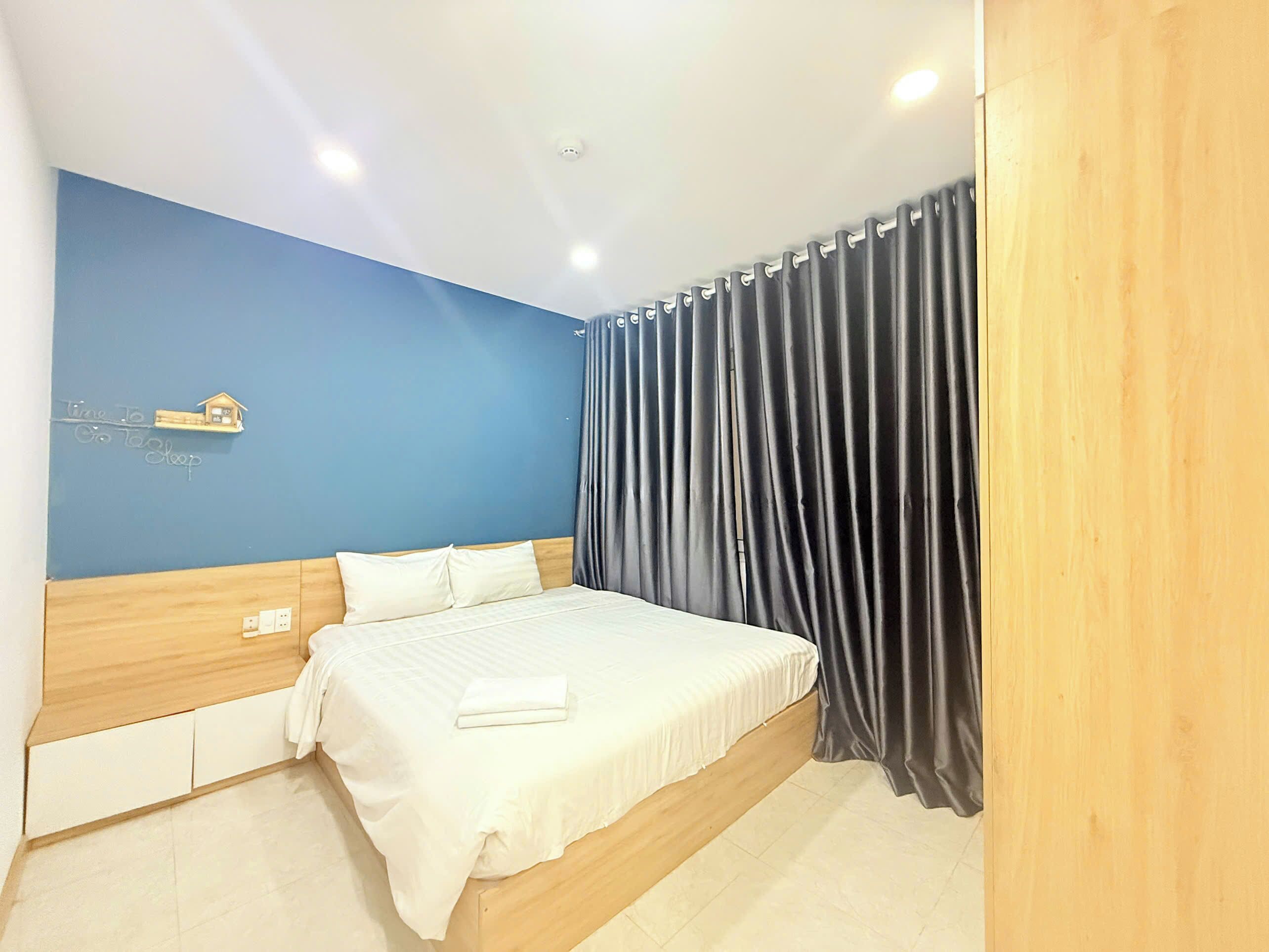 Ein Hotelzimmer mit einem Bett, einer blauen Wand, einem hölzernen Kopfteil und einem Vorhang.