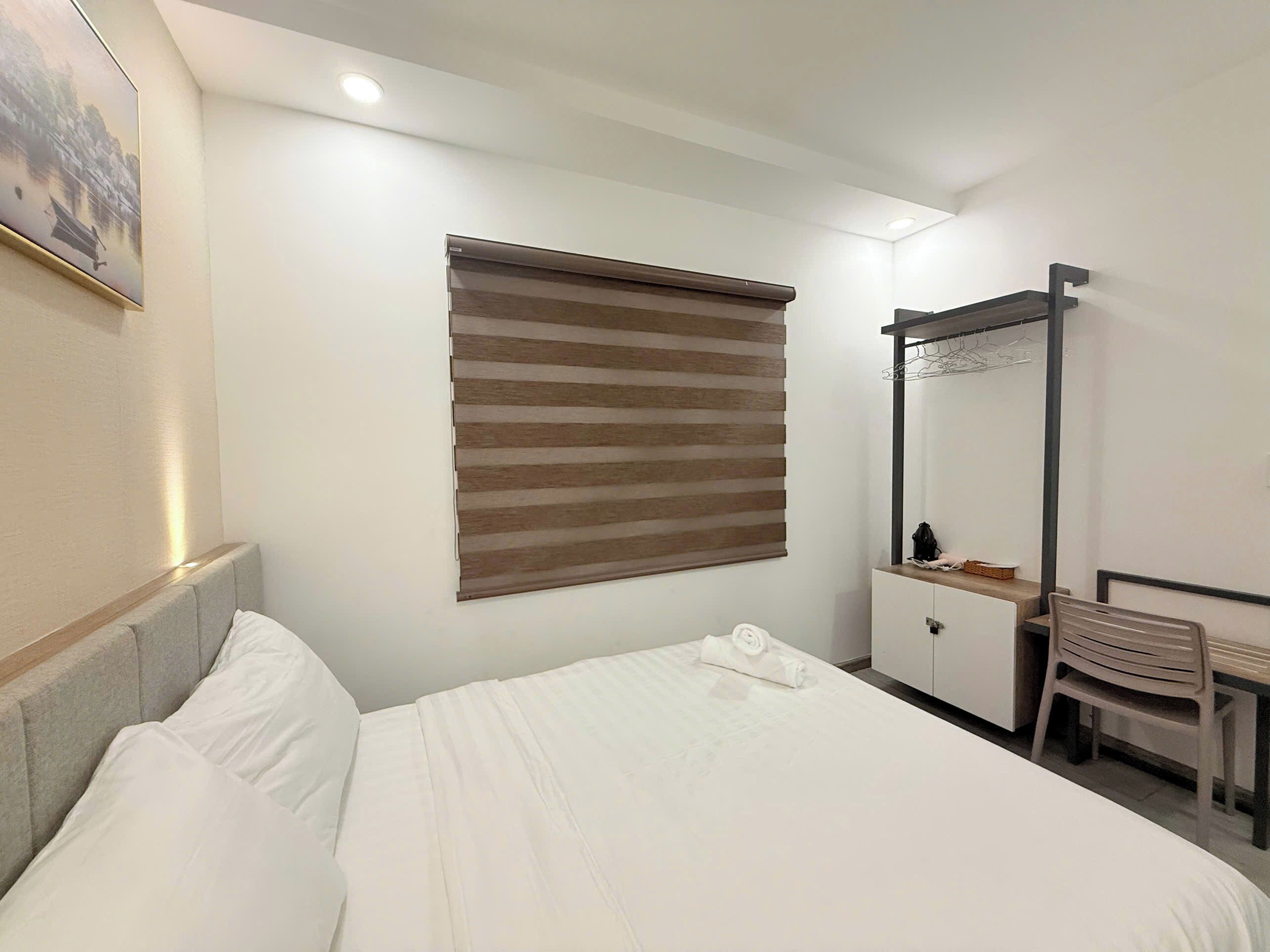 Een hotelkamer met een bed, een raam met jaloezieën, een spiegel, een kledingkast en een stoel.