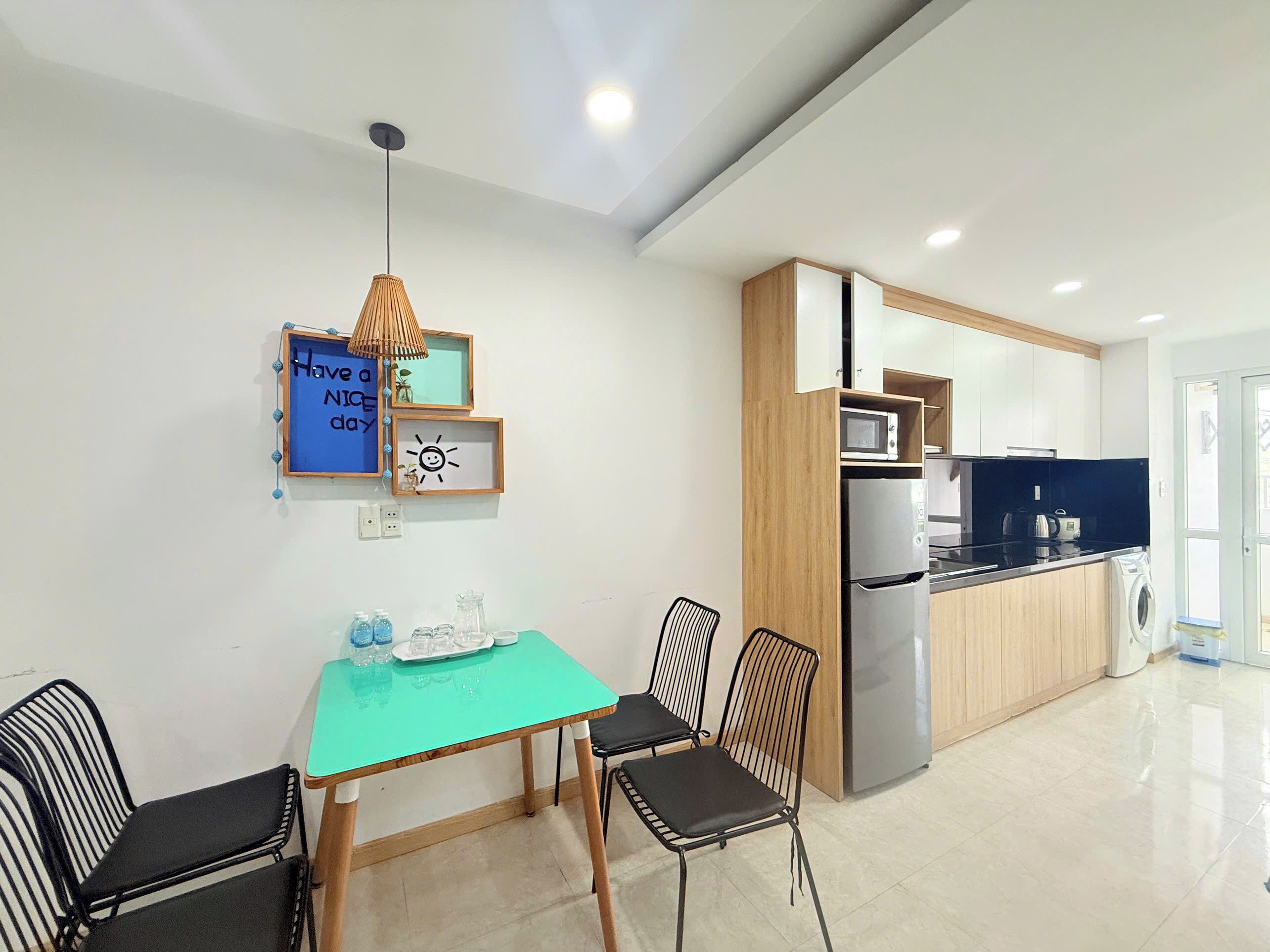 A modern kitchen with a built-in microwave, refrigerator, and washing machine. There is a dining area with a table and chairs.