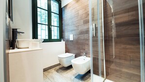 Un baño moderno con ducha de vidrio, inodoro, bidé, lavamanos y ventana.