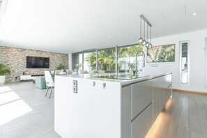 Une cuisine moderne dotée d’un grand îlot central, d’un mur en pierre et d’un téléviseur à écran plat.