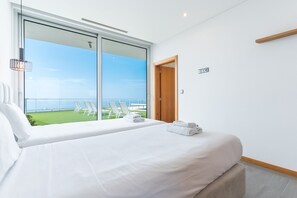 A hotel room with a large sliding glass door leading to a balcony with a view of the sea. There is a bed with white linens and two towels on it. - Villa Vista Atlântica by Atlantic Holiday (Ribeira Brava)