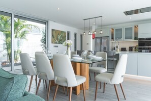 A modern kitchen with a central island, dining area with chairs, and a view of the outdoors. - Villa Vista Atlântica by Atlantic Holiday (Ribeira Brava)