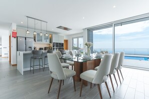 Une cuisine moderne dotée d’un îlot central, de tabourets de bar et d’un coin repas avec une table et des chaises en verre.