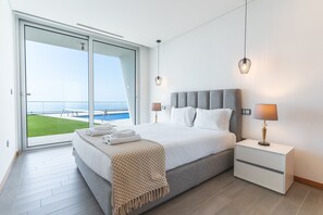 Une chambre moderne avec un grand lit, une table de chevet et une vue sur une piscine et le ciel.