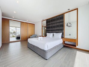 A modern bedroom with a large bed, a wooden wardrobe, a seating area, and a balcony with a view. - Villa Vista Atlântica by Atlantic Holiday (Ribeira Brava)
