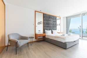 A modern bedroom with a large bed, a chair, a nightstand, and a view of the ocean. - Villa Vista Atlântica by Atlantic Holiday (Ribeira Brava)