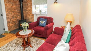 A living room with a brick wall, a red sofa, a small round table with a vase, a lamp, and a fireplace. - Frog Leap (Scunthorpe)