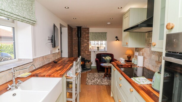 A compact kitchen with a wooden countertop, a built-in stove, and a small dining area with a chair and table. - Frog Leap (Scunthorpe)