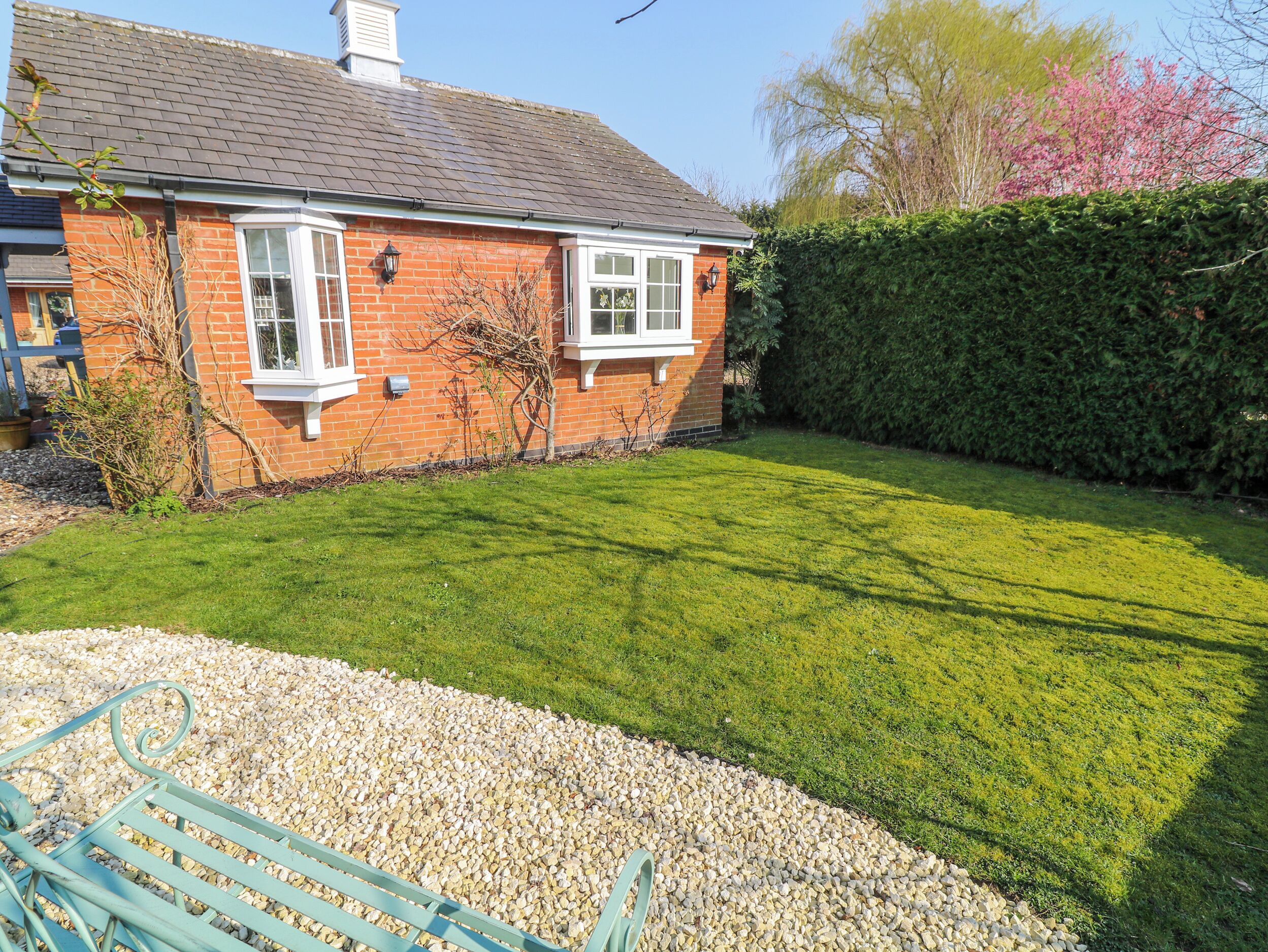 A brick house with a well-maintained lawn, a hedge, and a gravel path leading to a bench.